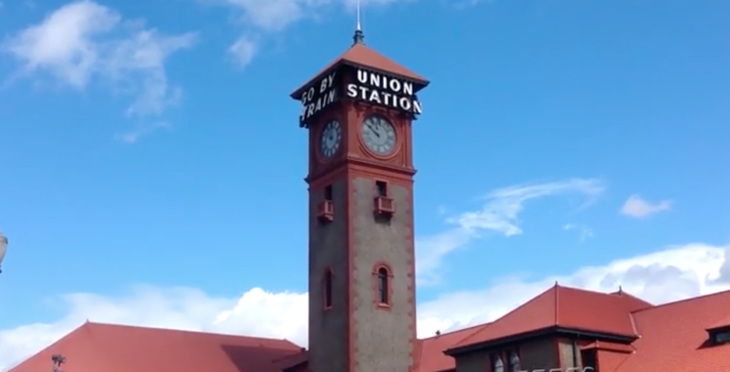Stone or brick tower and red roof of a train station in sunshine.