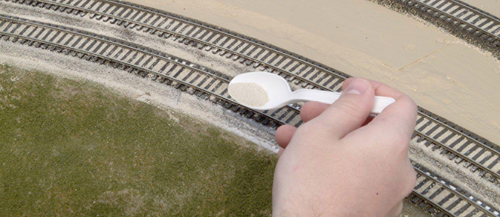 An image of a spoon held above model railroad track.