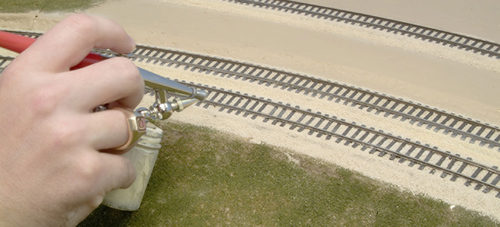 An airbrush is shown used on a model railroad layout.