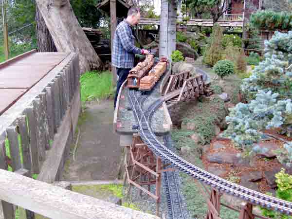 man next to elevated tracks, servicing model steam engine