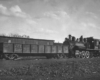 A black and white photo of a steam locomotive dropping off a gondola car