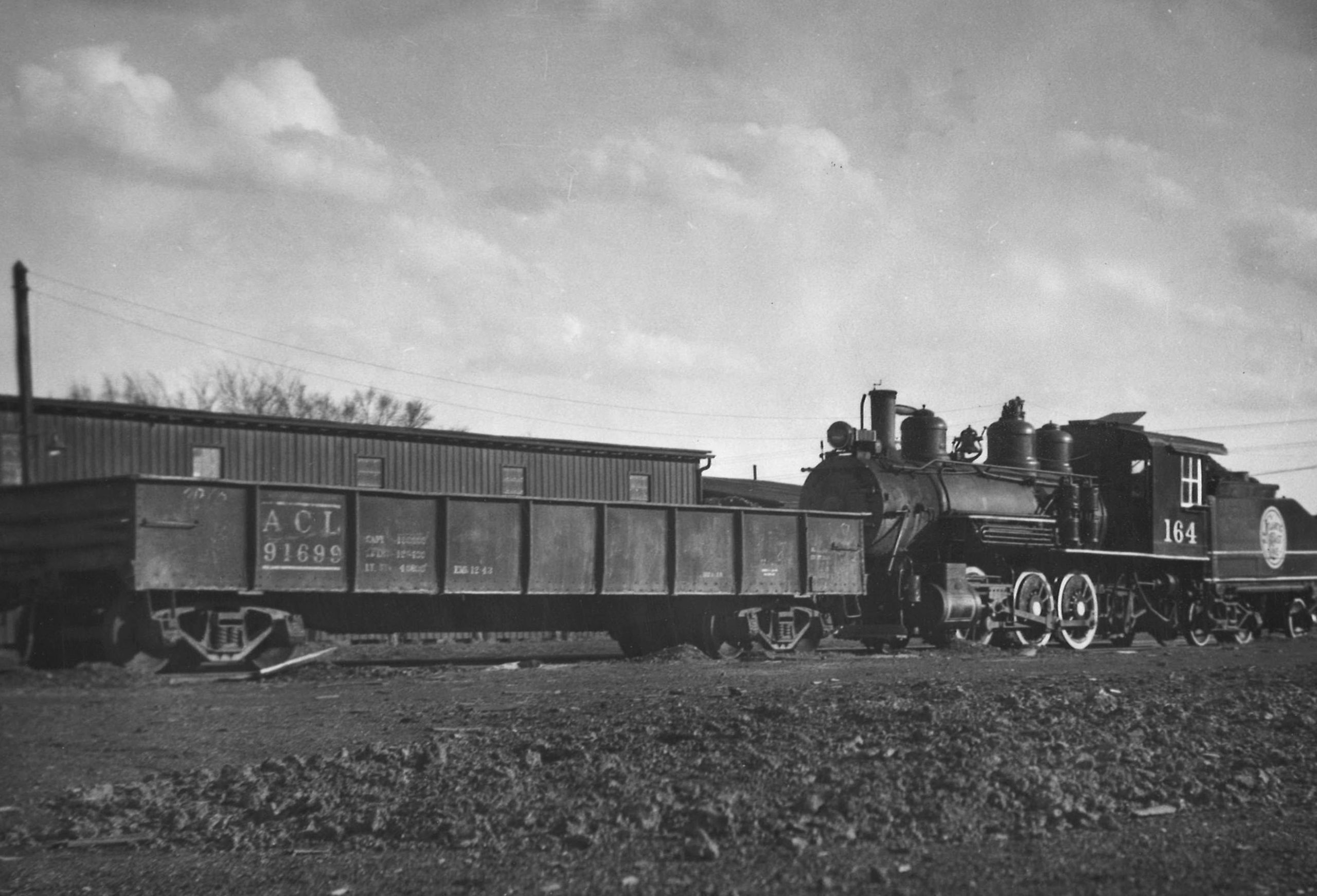 A black and white photo of a steam locomotive dropping off a gondola car