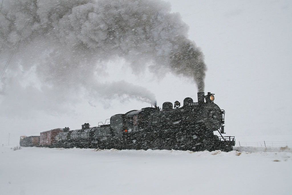 A train plowing through the snow with smoke coming out of its chimney