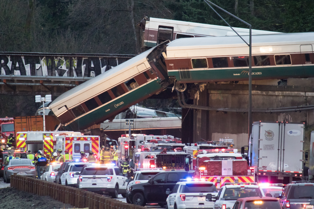 Passenger cars of derailed train hanging off bridge over highway
