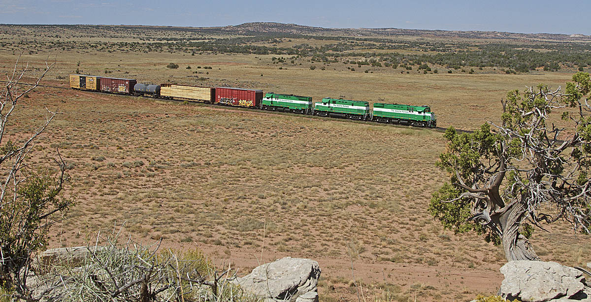 Green diesel locomotives pulling short freight train across the desert