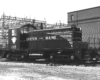 A black and white photo of an EMD switching-type locomotive sitting on the tracks in front of a building