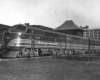 A black and white photo of an EMD locomotive sitting on the tracks in front of buildings 