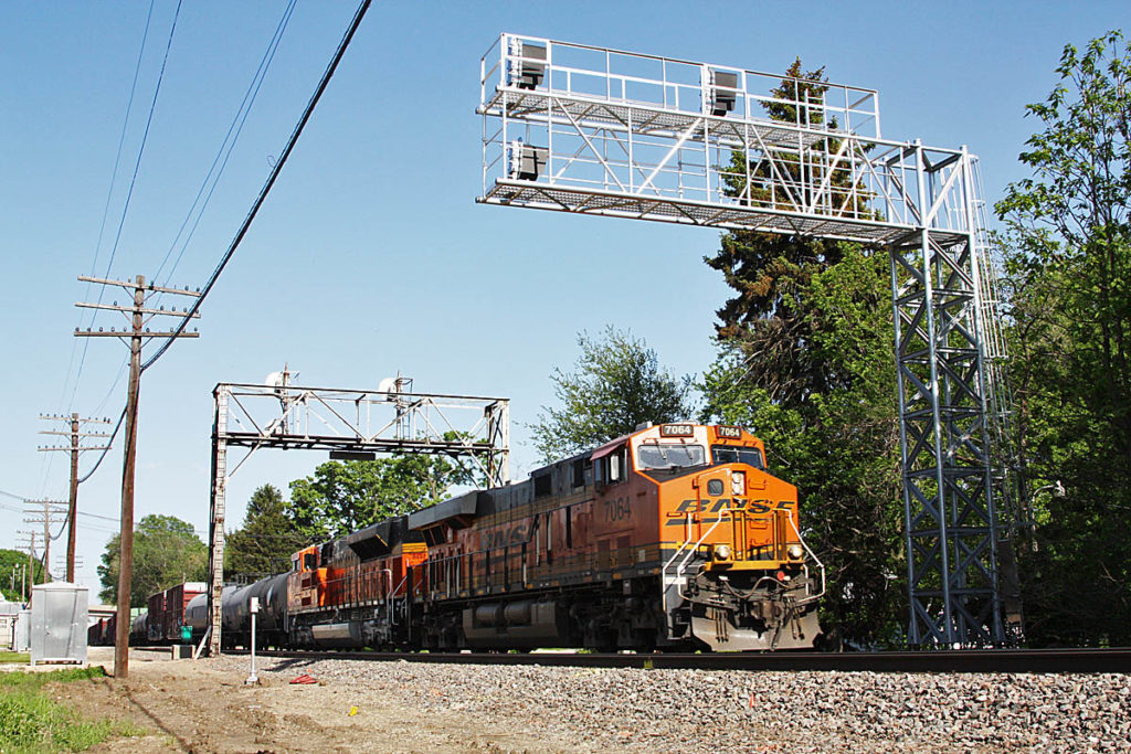 Orange and green diesel locomotive passes under signal bridge. Glossary of railroad signal terminology