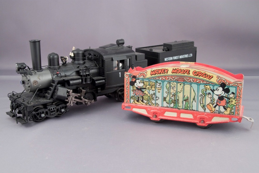 A detailed Climax logging locomotive model next to an old-looking circus car with few details and printed sides showing a caged elephant and Mickey and Minnie Mouse.