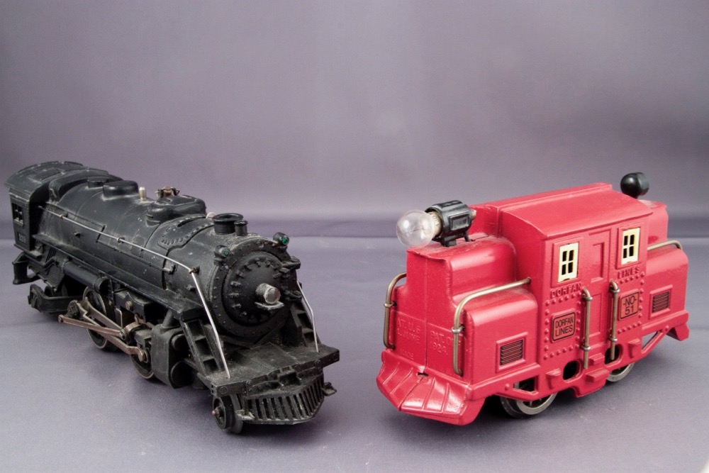 A black-colored Lionel steam locomotive is on the left, with a red Dorfan locomotive on the right looking like an early 1900s electric freight motor.