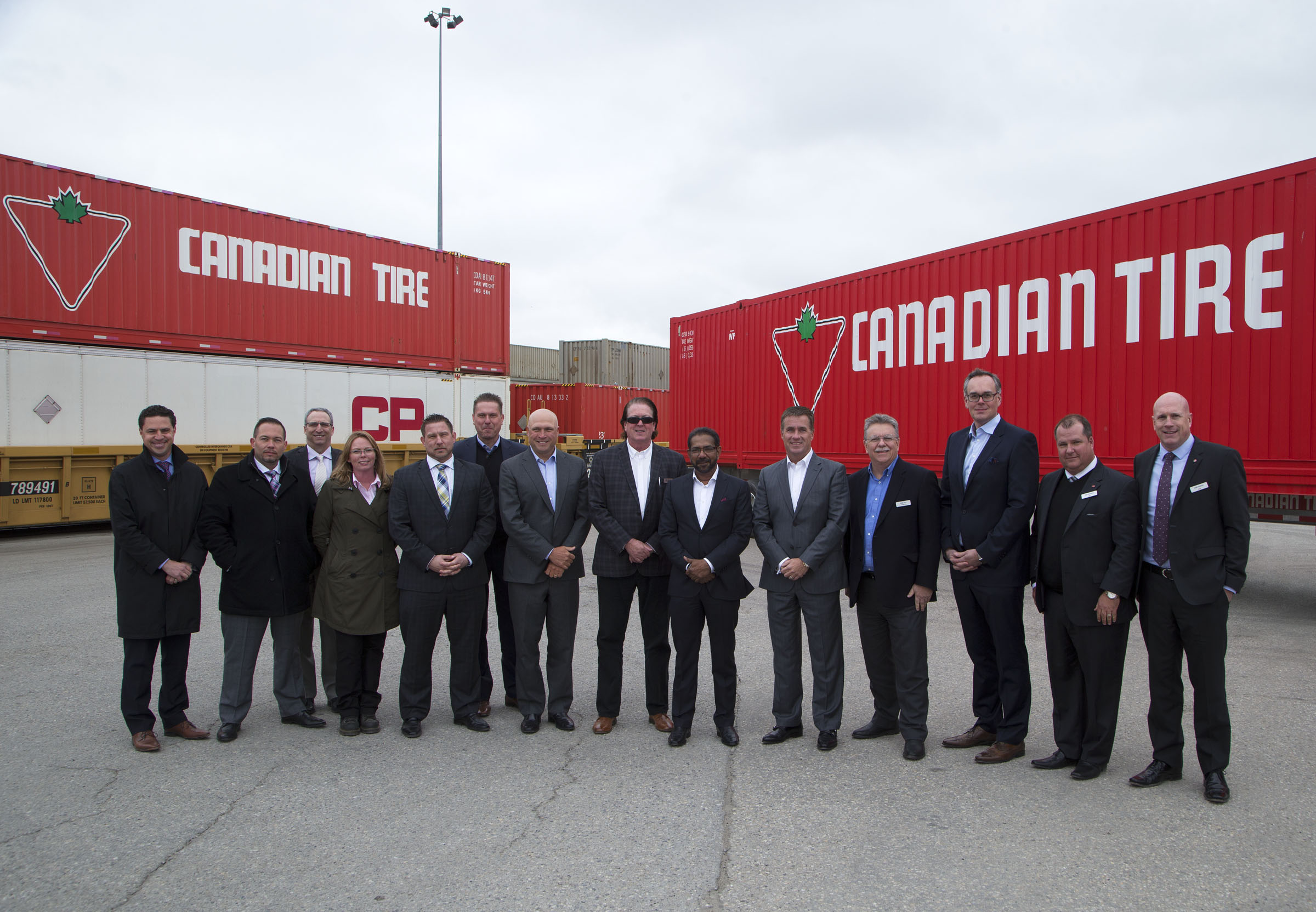 Fourteen people standing in front of red and white containers on train and truck