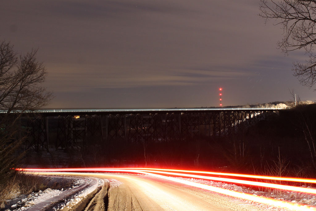 A distant shot of a lit train passing over a bridge in the dark