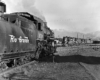 A black and white close up of a steam locomotive approaching a diesel locomotive on the tracks.