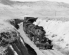 A black and white photo of a 2-8-8-2 steam locomotive moving between two hills