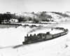 A black and white photo of a 2-8-2 steam locomotive turning the corner on the tracks on a snowy day