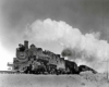 A close up shot of a train with big white smoke coming out of its chimney