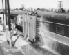 A passenger car by a tall metal box that's spraying water onto it