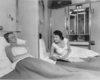 A couple of women laying in their beds talking through an open partition