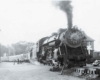 A black and white photo of people walking by a train