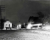 A black and white photo of a passenger train passing a station in the dark