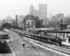 A black and white photo of a train passing through a busy city