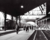 A black and white photo of people walking through a train station 