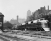 A black and white photo of a train parked outside a city