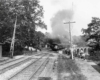 A black and white photo of a train exiting a tunnel with workers on the side