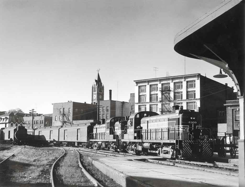 a diesel passenger train in front of buildings