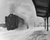 a steam engine passenger train at a passenger depot on a snowy day