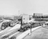 Two steam-powered passenger trains pass diesel switcher under bridges