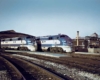 Two diesel powered passenger trains rest outside train shed