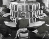 a group of women sitting at a circular table wearing headphones and plugging pegs into a switchboard