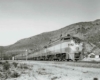 A black and white photo of a locomotive moving pass mountains
