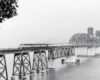 A distant black and white photo of a locomotive crossing a bridge