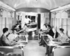 A black and white photo of passengers inside a coffee-shop lounge car