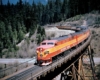 An orange and yellow locomotive turning the corner on a bridge