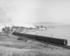 A black and white photo of a locomotive turning a corner next to a lake