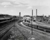 A black and white distant shot of a train station and locomotives in a rail yard