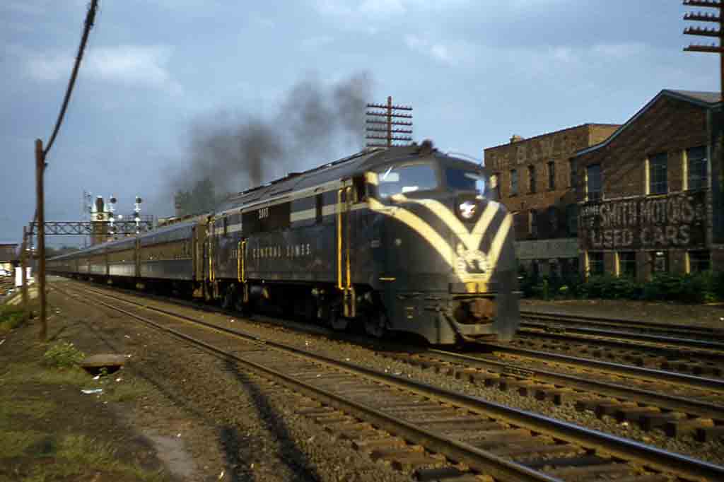 A black train with yellow stripes passing by buildings