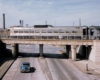 A locomotive travels over a bridge as a car travels below the bridge at the same time