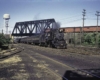 A locomotive moving down the tracks with a water tower in the background