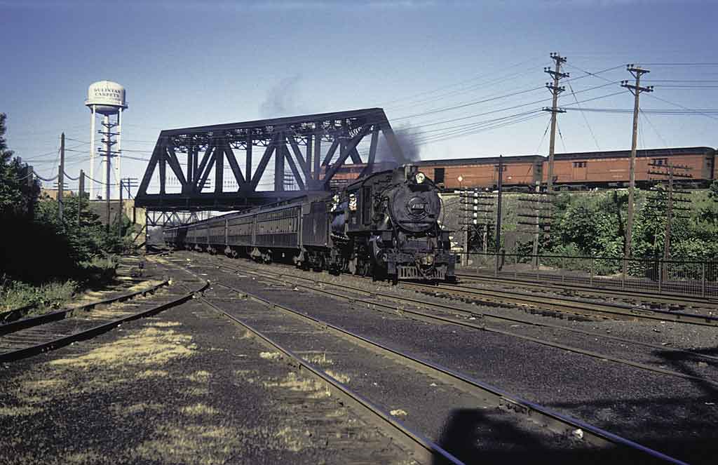 A locomotive moving down the tracks with a water tower in the background