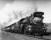 A black and white photo of a train coming down the tracks with white smoke coming out of its chimney