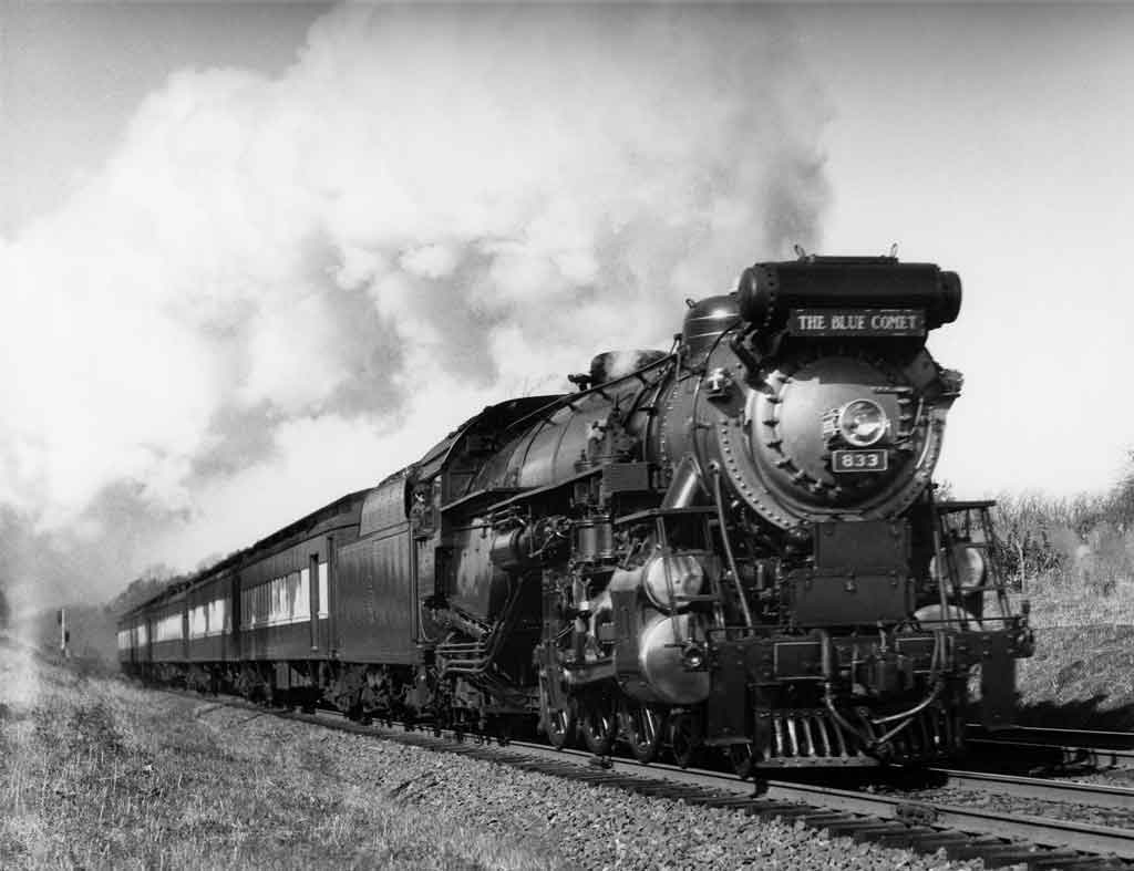 A black and white photo of a train coming down the tracks with white smoke coming out of its chimney