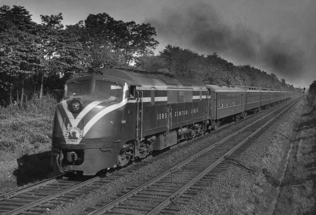 A black and white photo of a training moving down the tracks next to trees