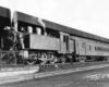 A black and white photo of a train outside a station