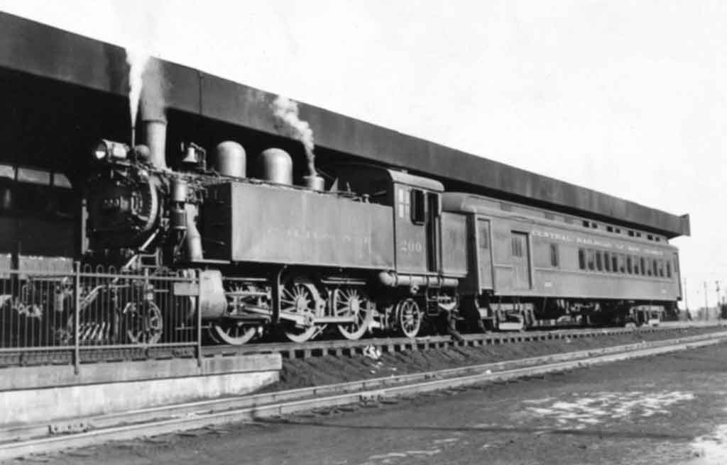 A black and white photo of a train outside a station