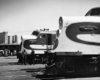 A black and white profile view of two trains with workers nearby