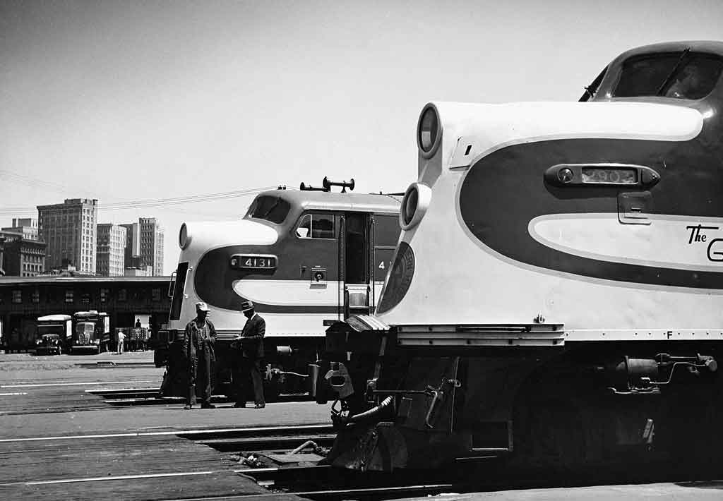 A black and white profile view of two trains with workers nearby